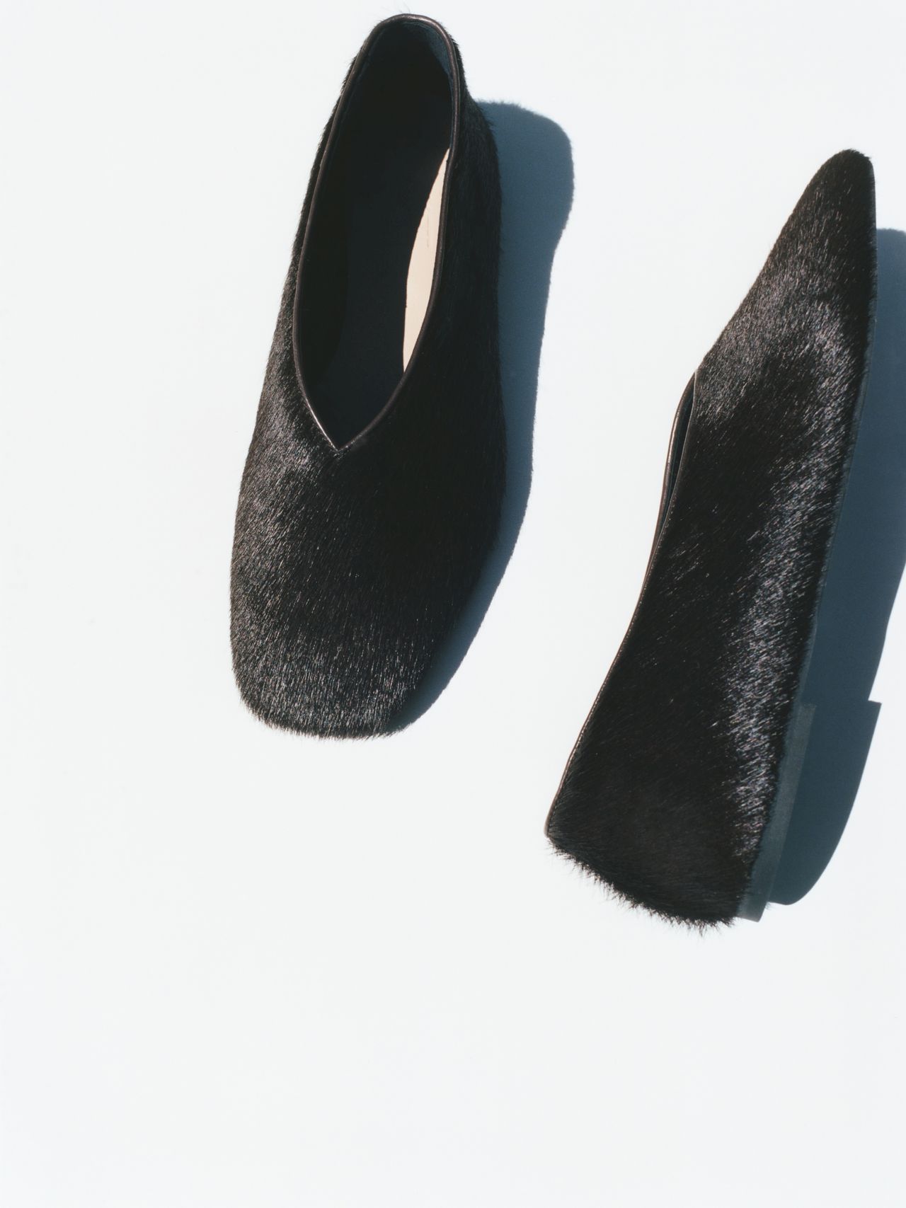 Two black fur-textured slip-on shoes on a white background, one shoe upright and the other on its side.