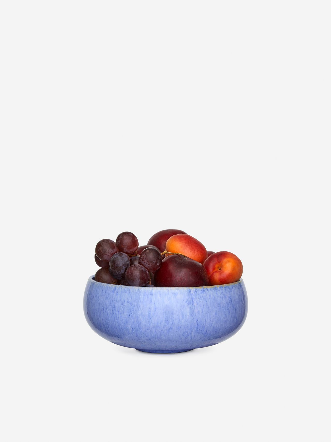 A blue bowl filled with red grapes and nectarines against a plain white background.
