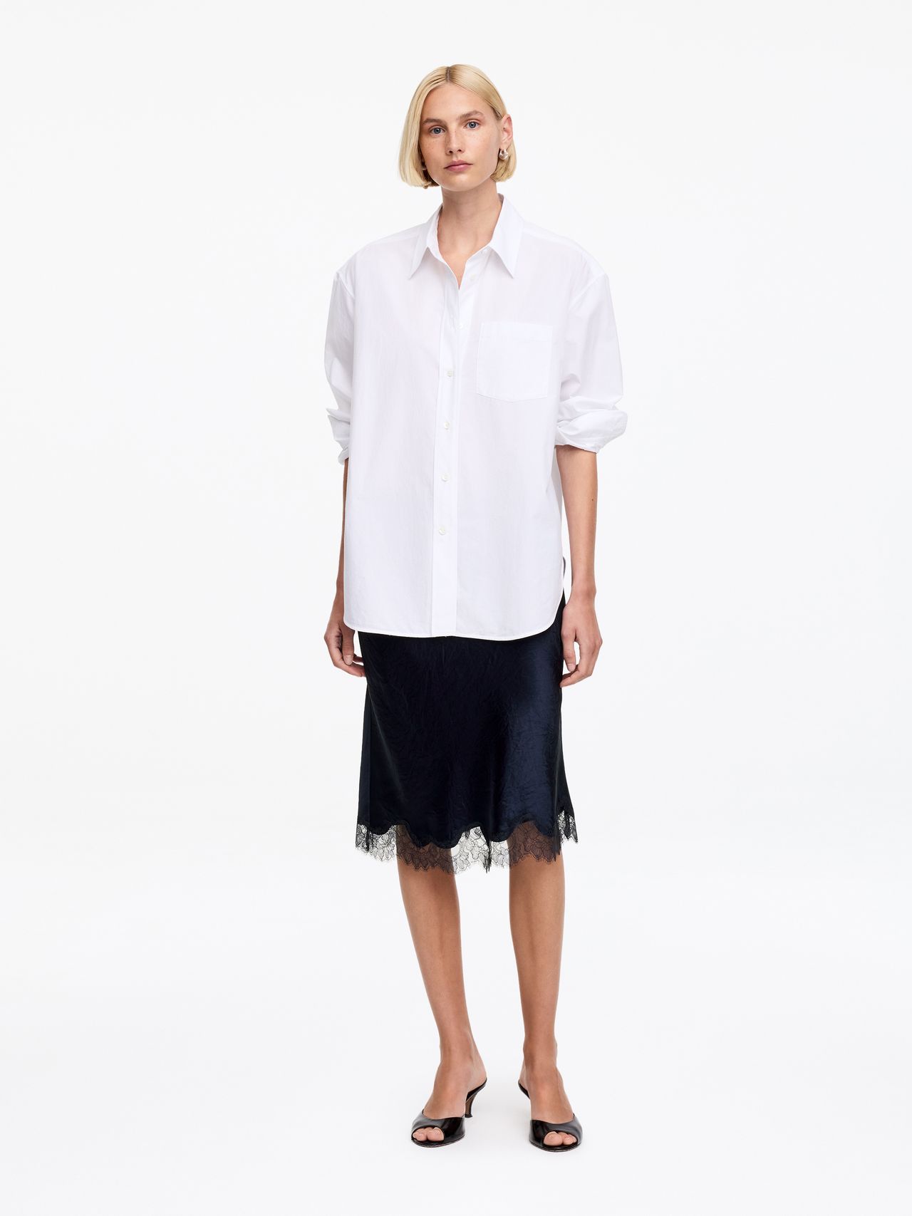 Person in a white button-up shirt and black lace-trim skirt with black sandals, standing against a plain white background.