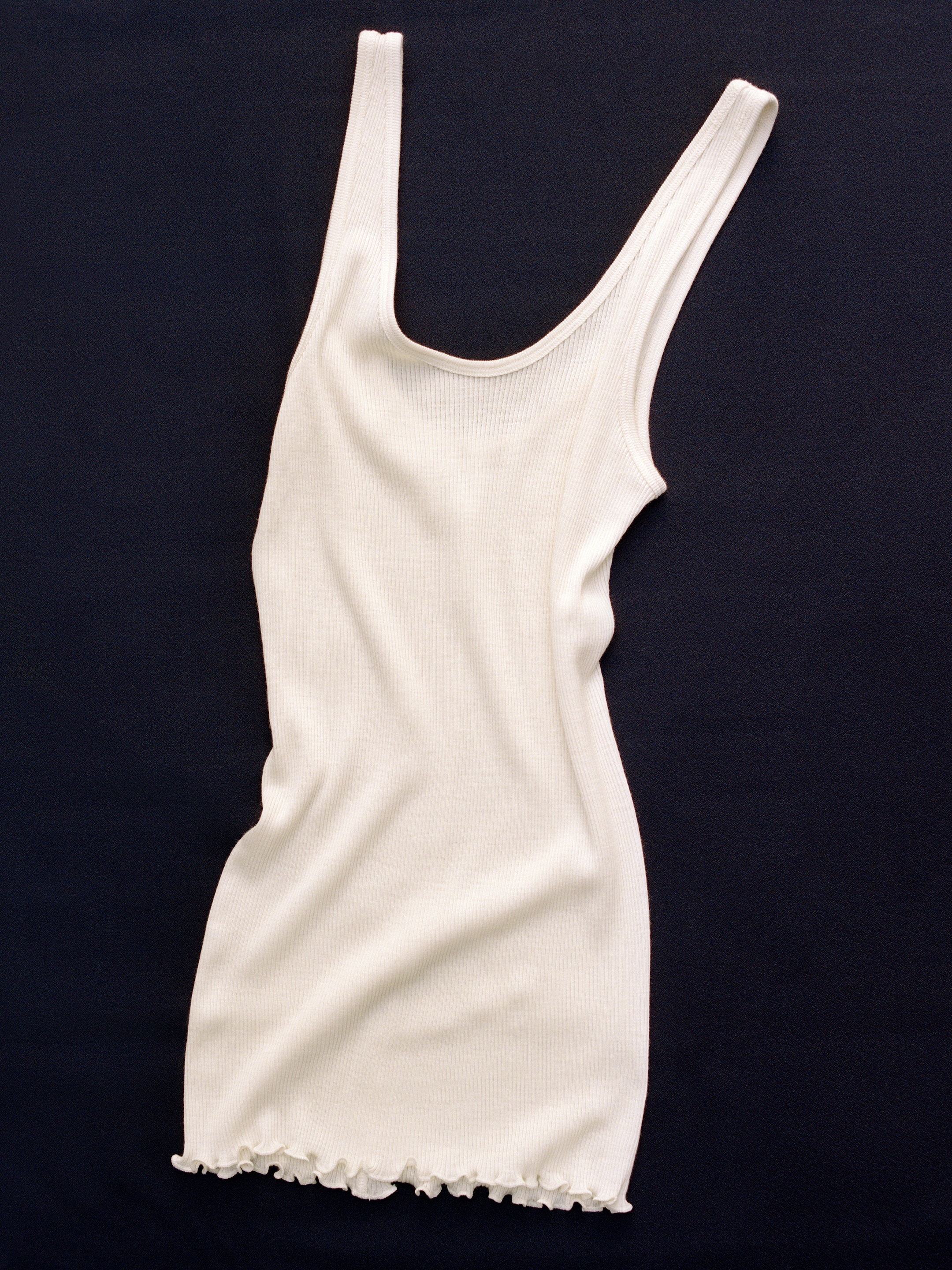 A white ribbed tank top with ruffled edges, laid flat on a dark surface.