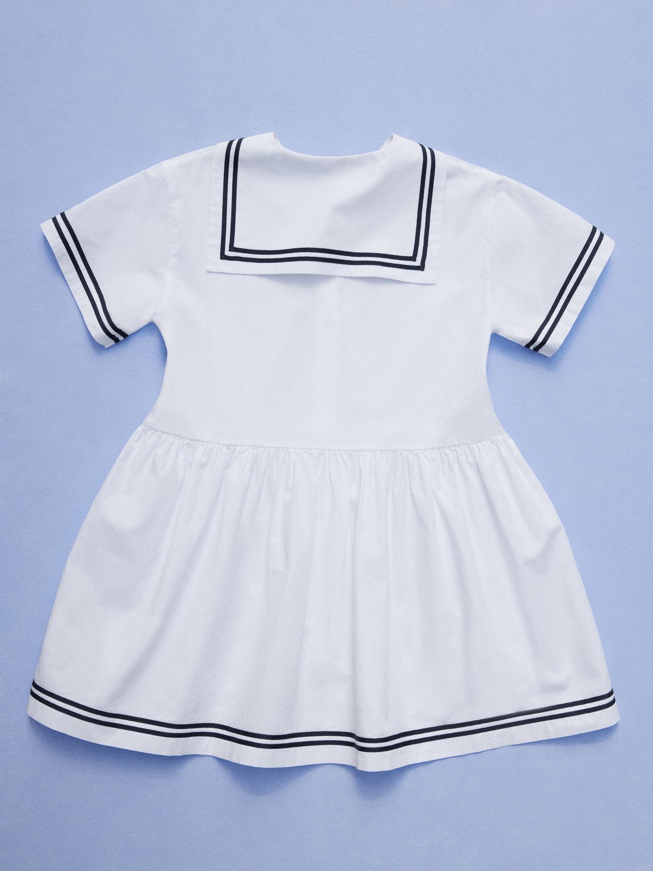 White sailor dress with navy trim on collar and hem, short sleeves, and pleated skirt, displayed on a light blue background.
