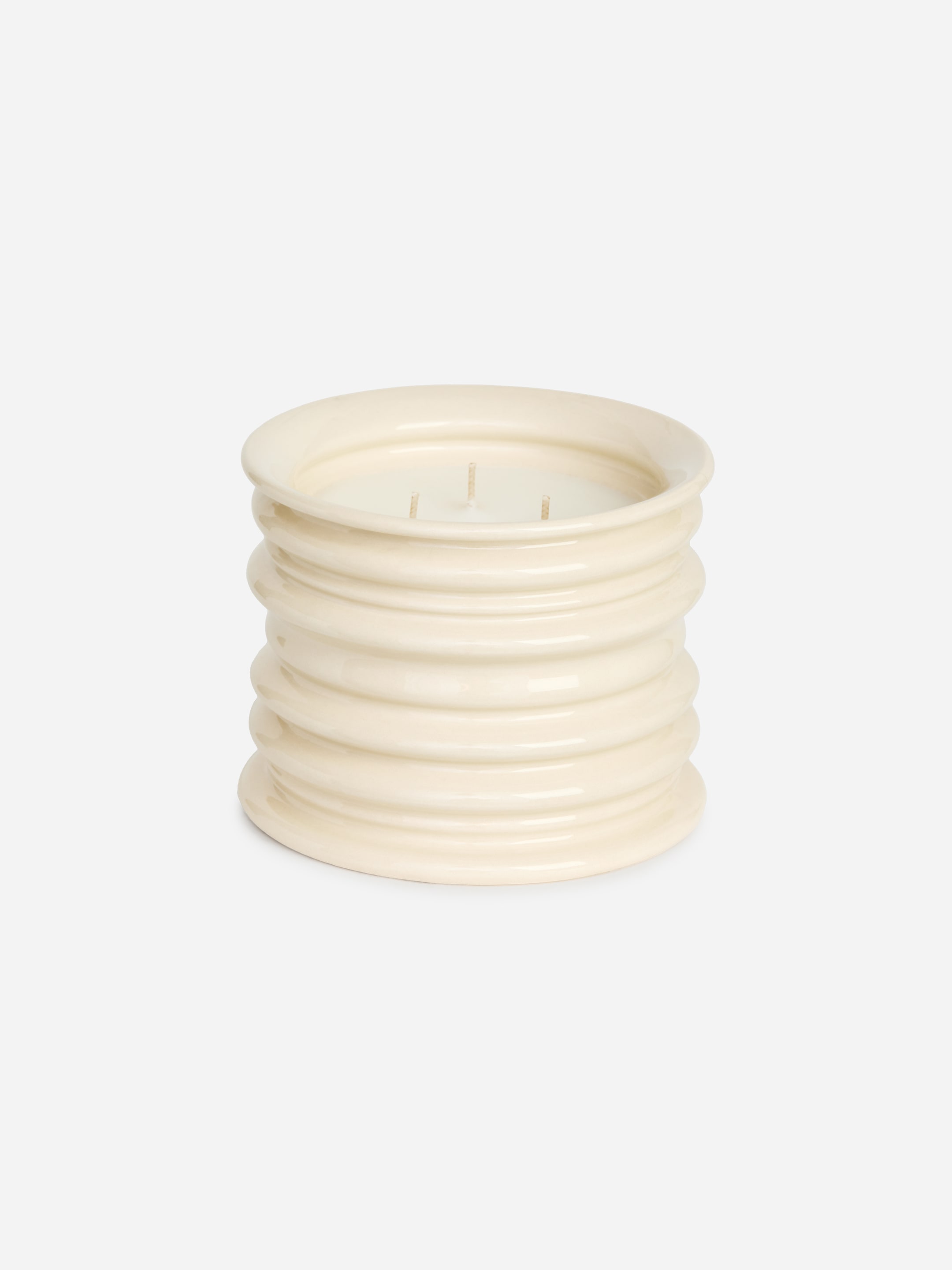 A cream-colored, ribbed ceramic candle holder with three visible wicks, set against a white background.