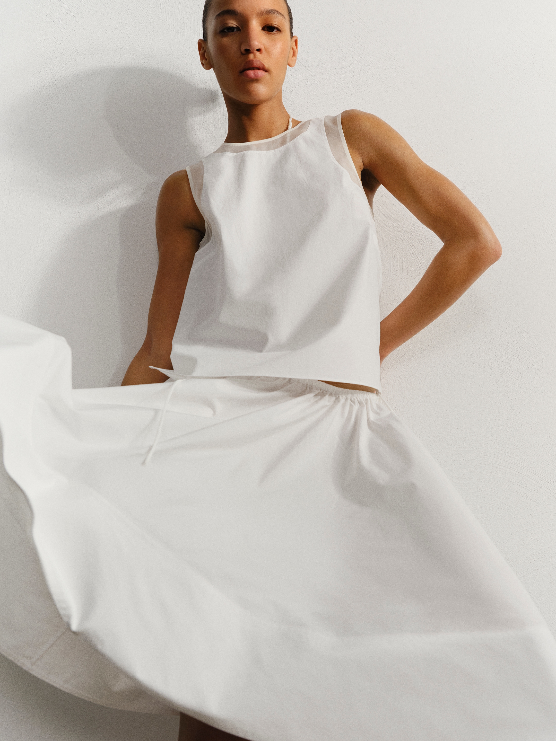 Person wears a sleeveless white dress, standing against a plain backdrop. The skirt flares gracefully with movement.