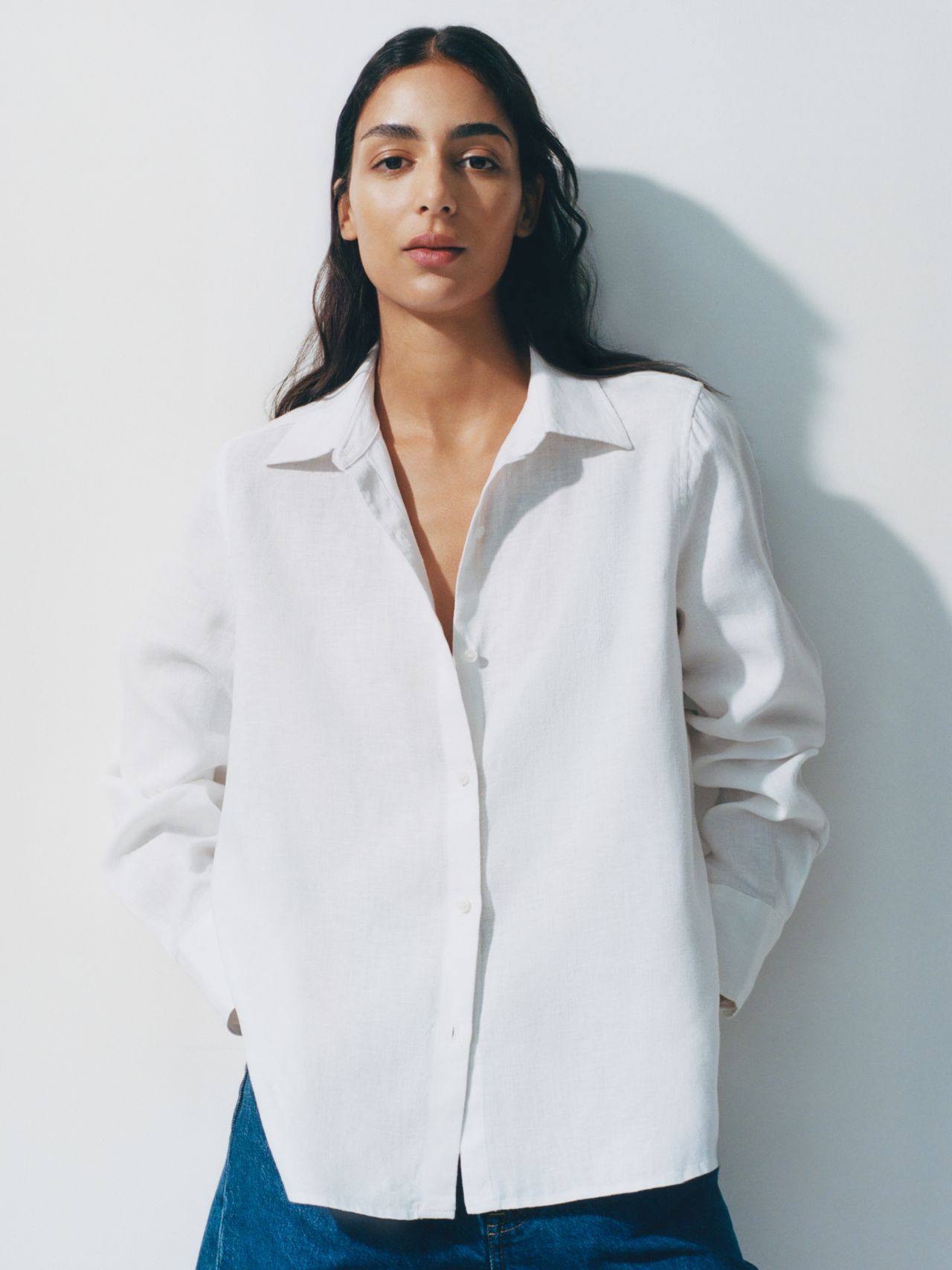 Person wearing a white button-up shirt and blue jeans, standing against a plain white background.