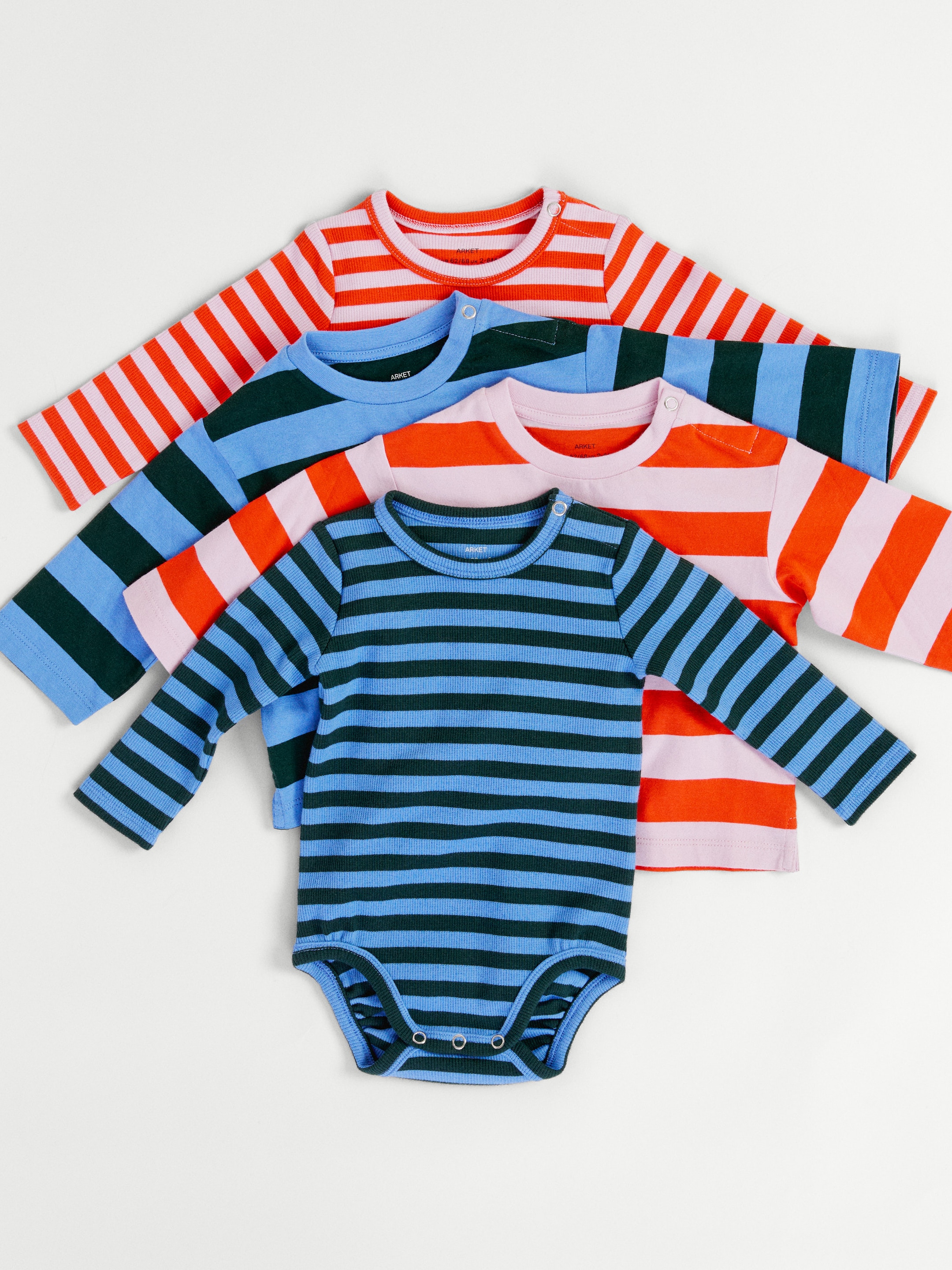 Four colorful striped baby onesies in different patterns, stacked on a white background.