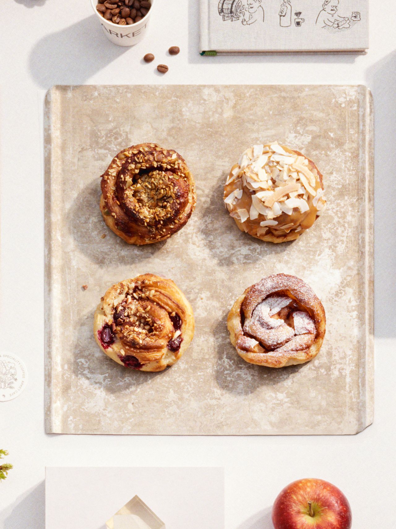 Four pastries on a baking sheet: one with nuts, one with coconut flakes, one with berries, and one dusted with powdered sugar.