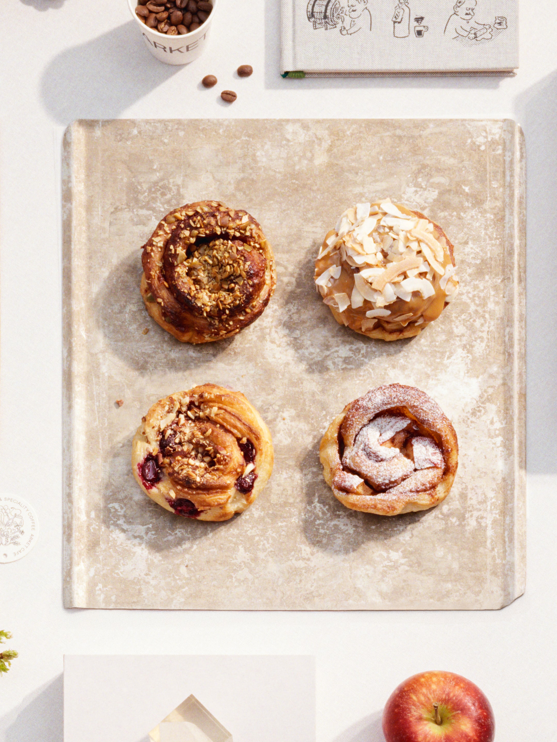 Four pastries on a baking sheet: one with nuts, one with coconut flakes, one with berries, and one dusted with powdered sugar.
