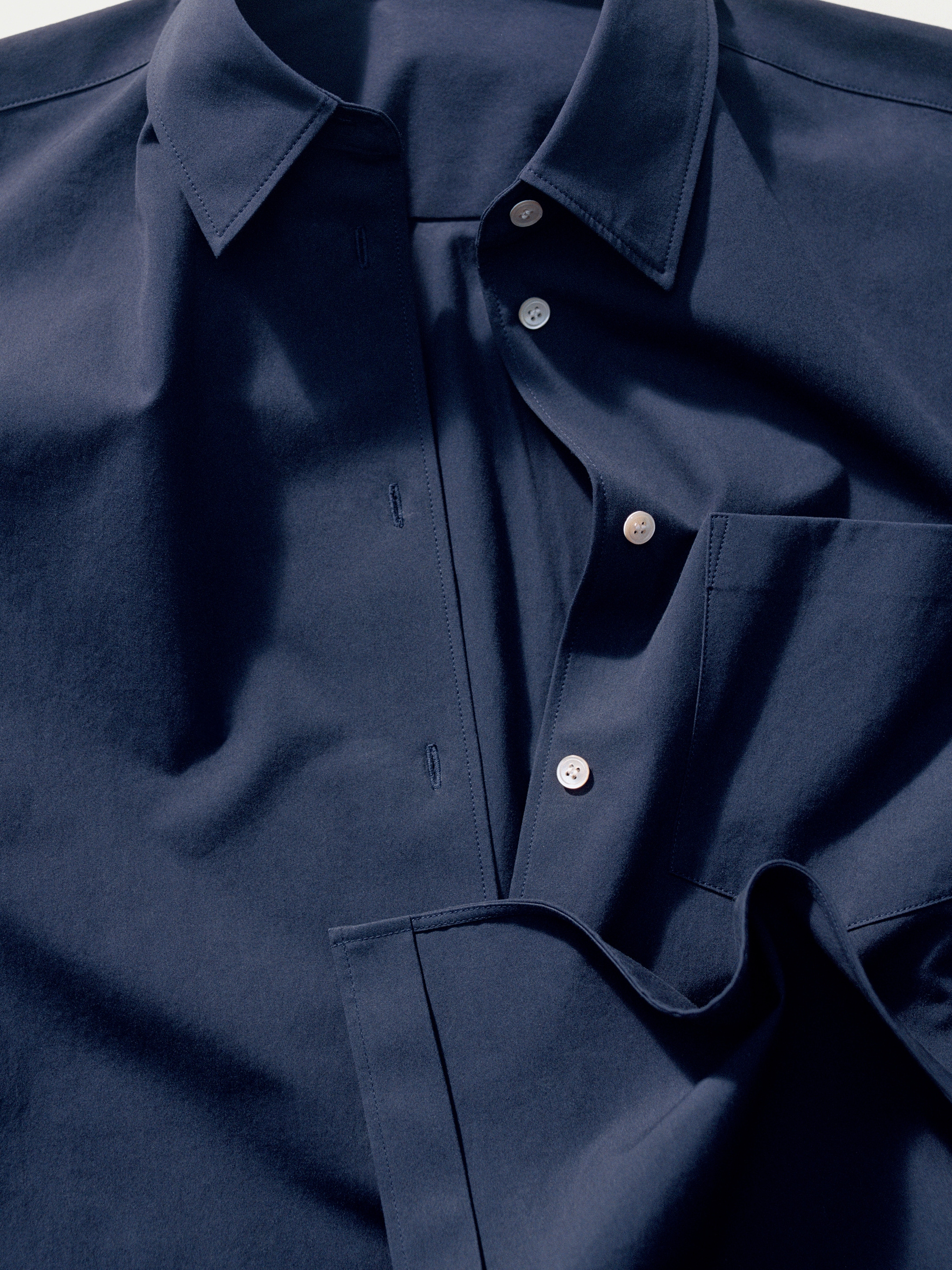Dark blue shirt with white buttons, partially unbuttoned and neatly folded. The fabric appears smooth and soft.