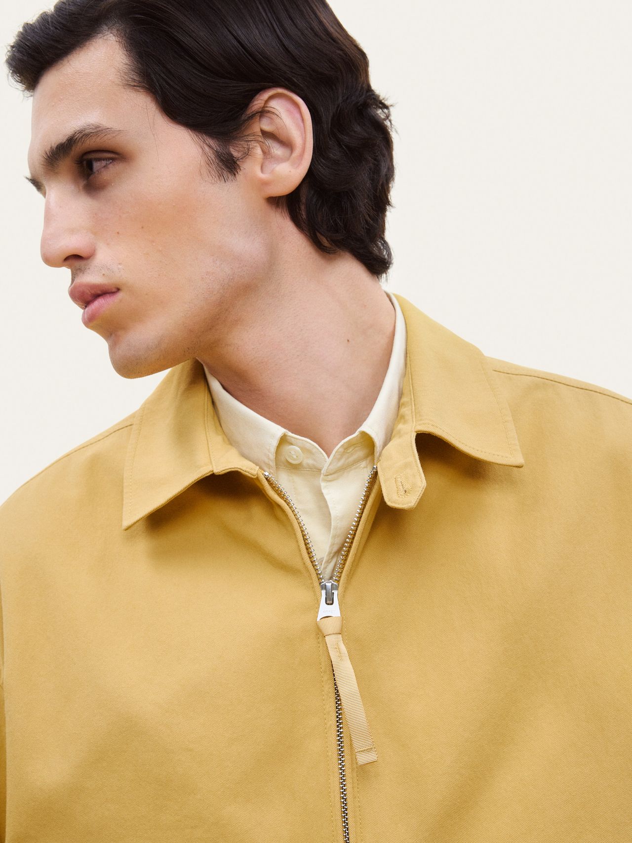 A person wearing a yellow jacket over a light shirt, looking to the side against a plain background.