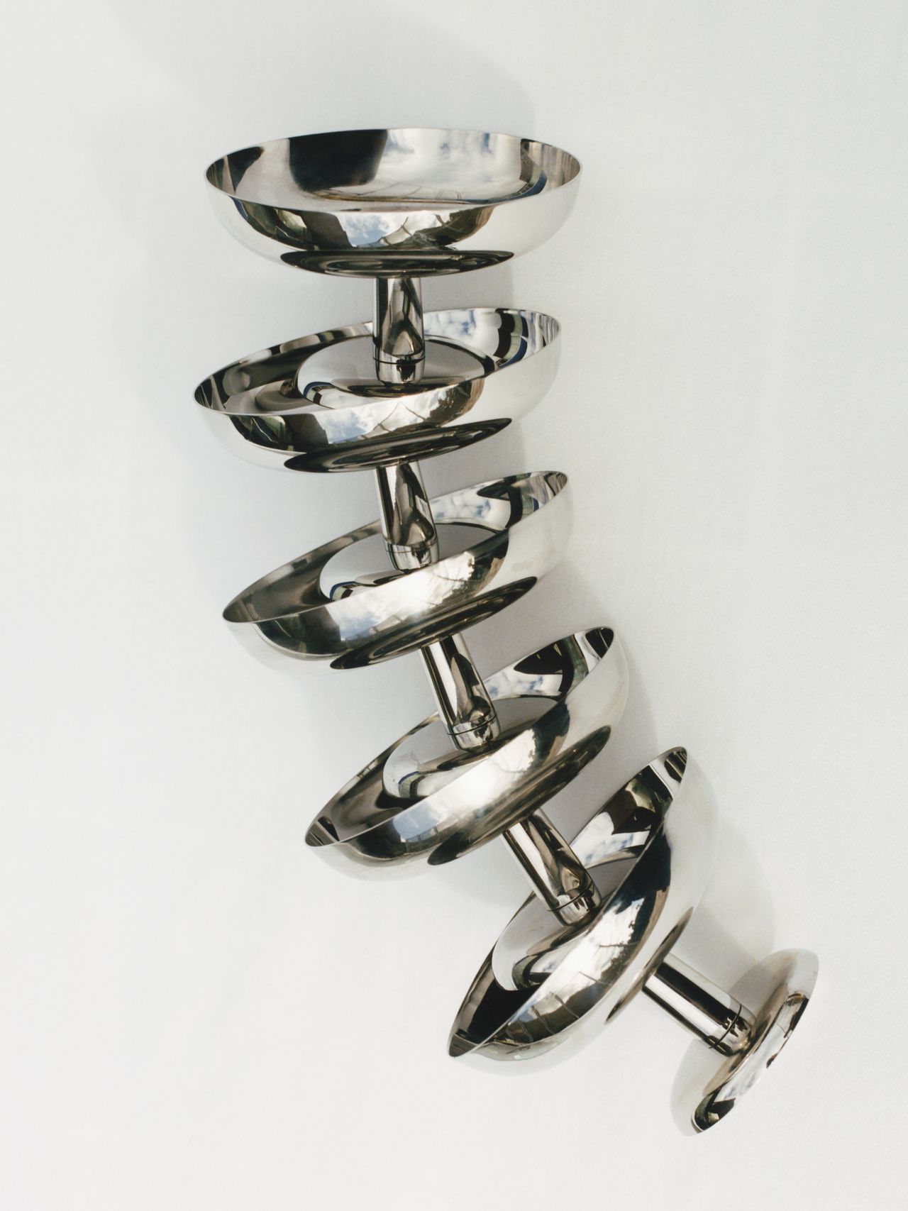 A sleek, modern metal sculpture with alternating concave discs stacked on a central rod, reflecting light against a plain white background.