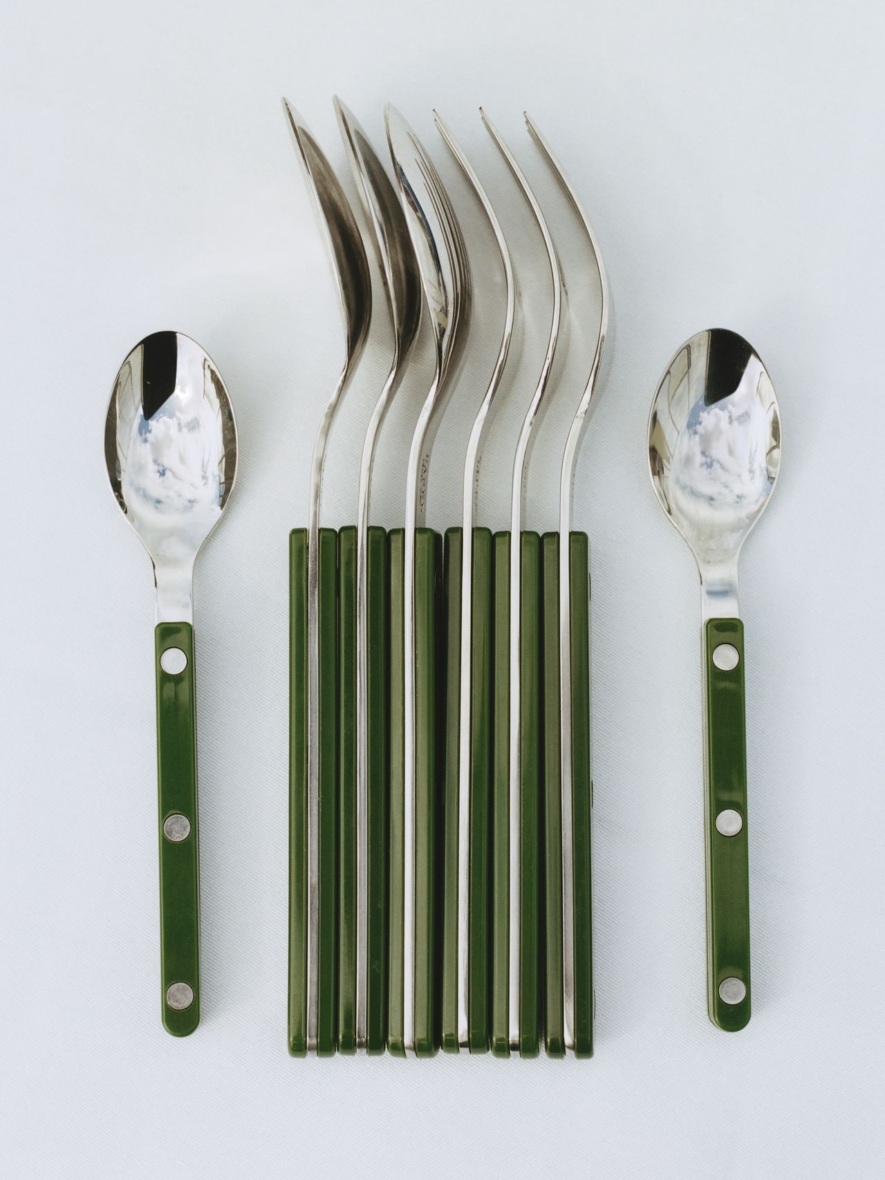 A set of spoons with polished metal heads and green handles arranged neatly on a white surface.