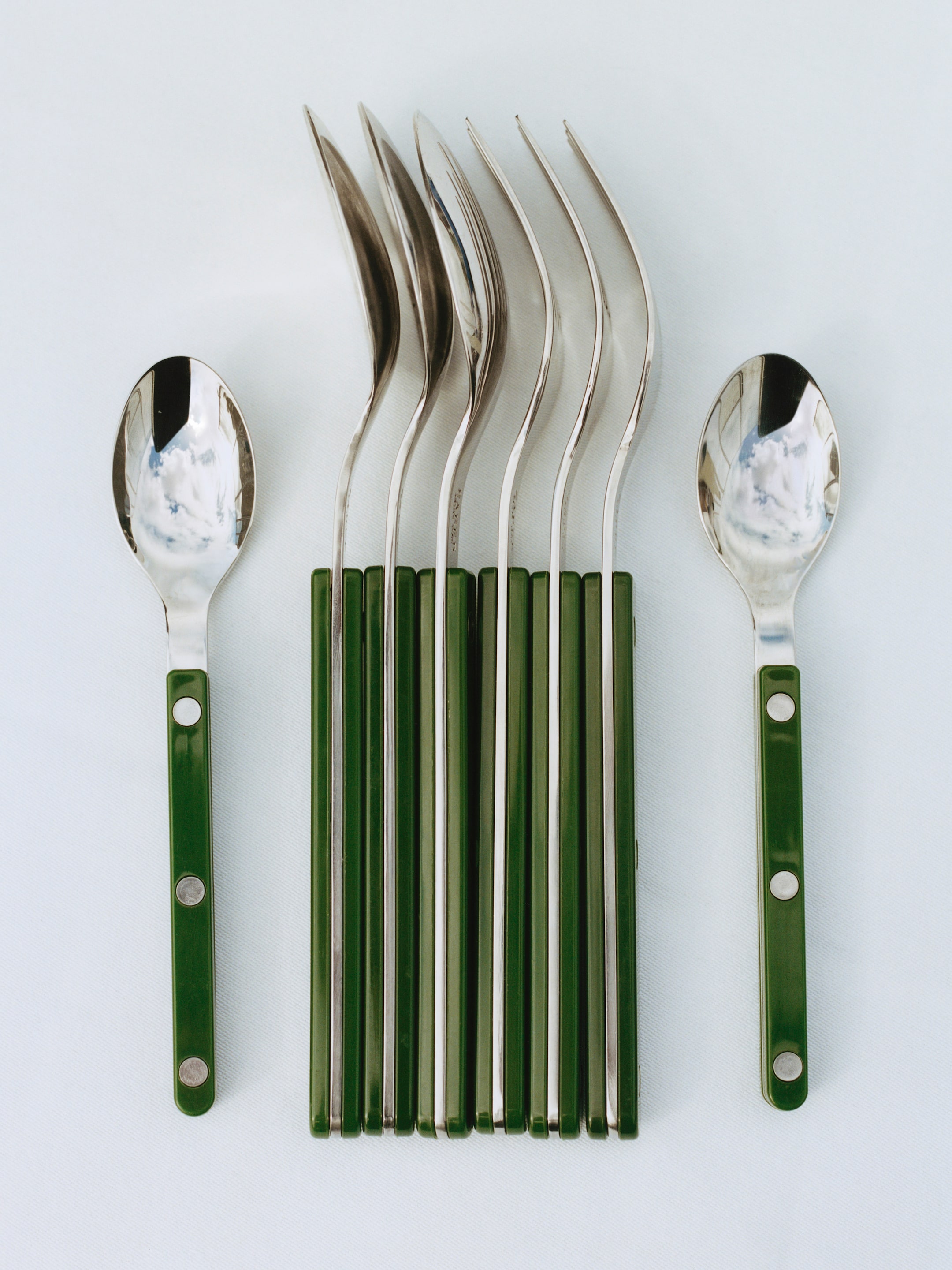 A set of spoons with polished metal heads and green handles arranged neatly on a white surface.