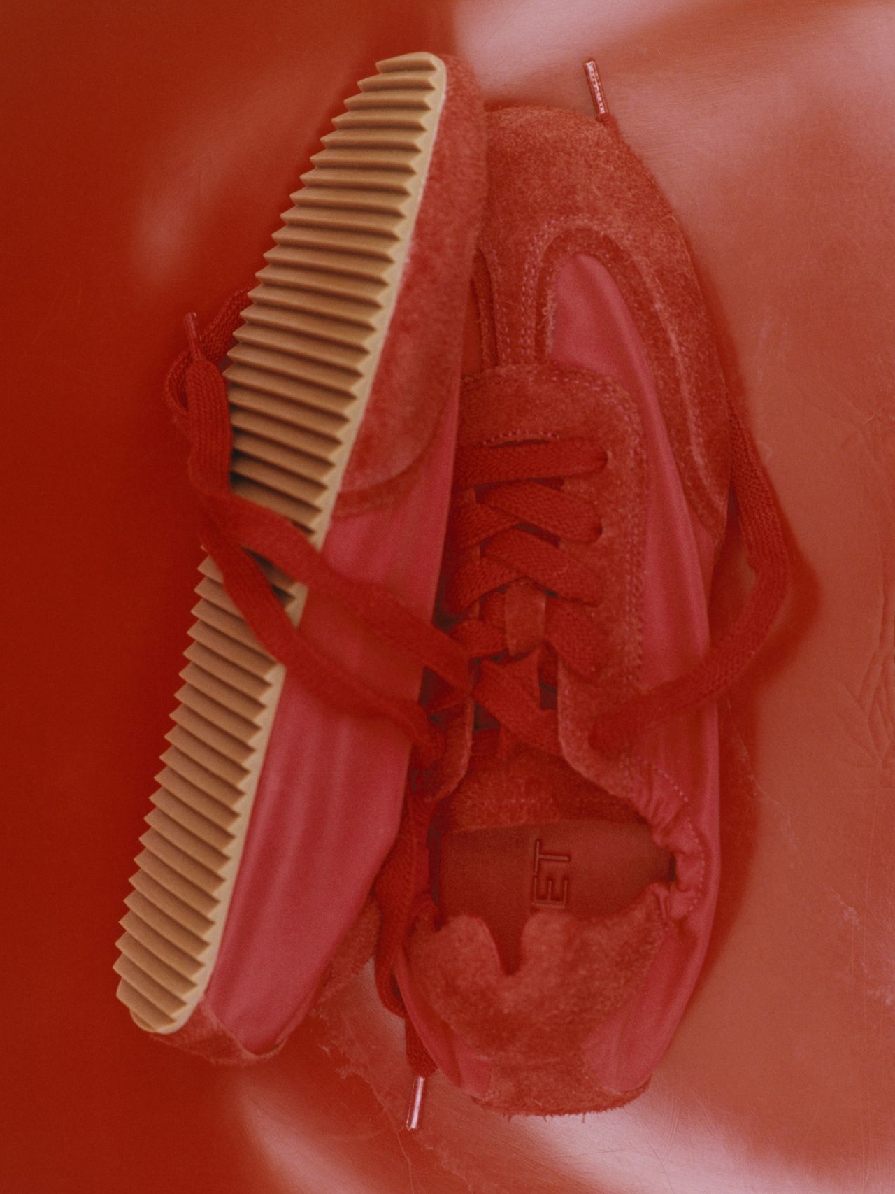Red sneakers with suede and smooth texture, featuring ribbed tan soles, placed on a red background.