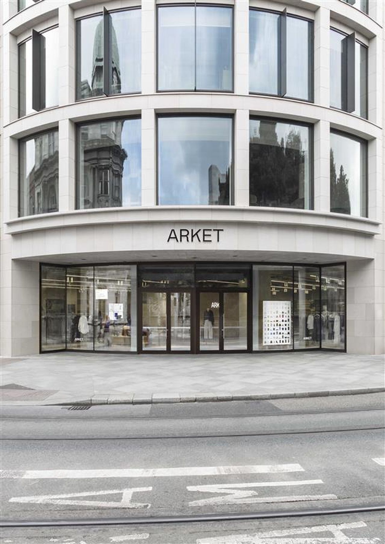Modern storefront of ARKET with large glass windows and entrance, set in a curved building facade, reflecting the surrounding cityscape.