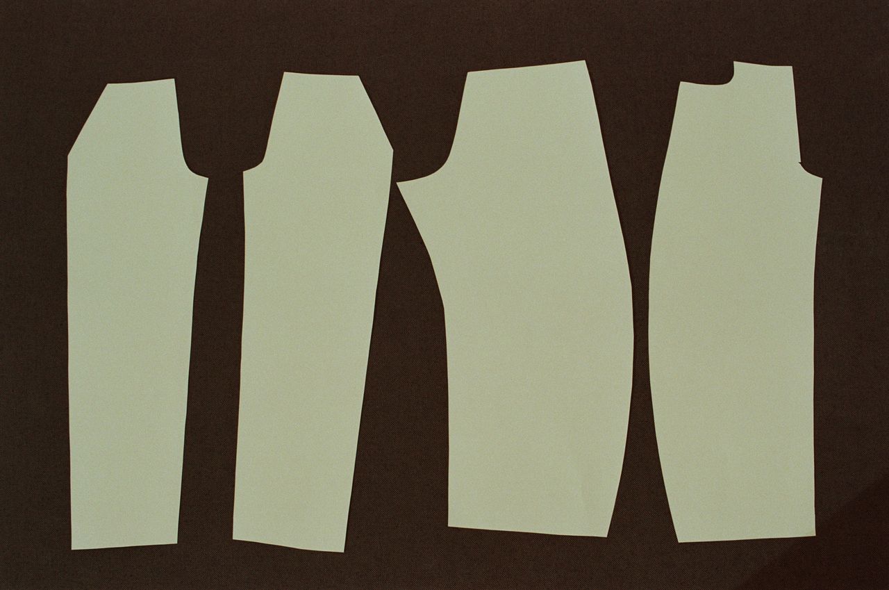 Four beige garment pattern pieces laid out on a dark brown background.