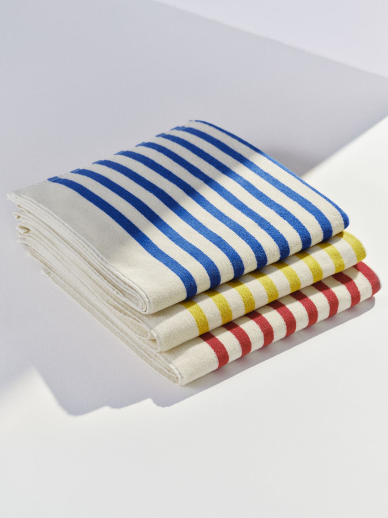 Folded towels stacked with blue, yellow, and red stripes on a white background, illuminated by natural light.