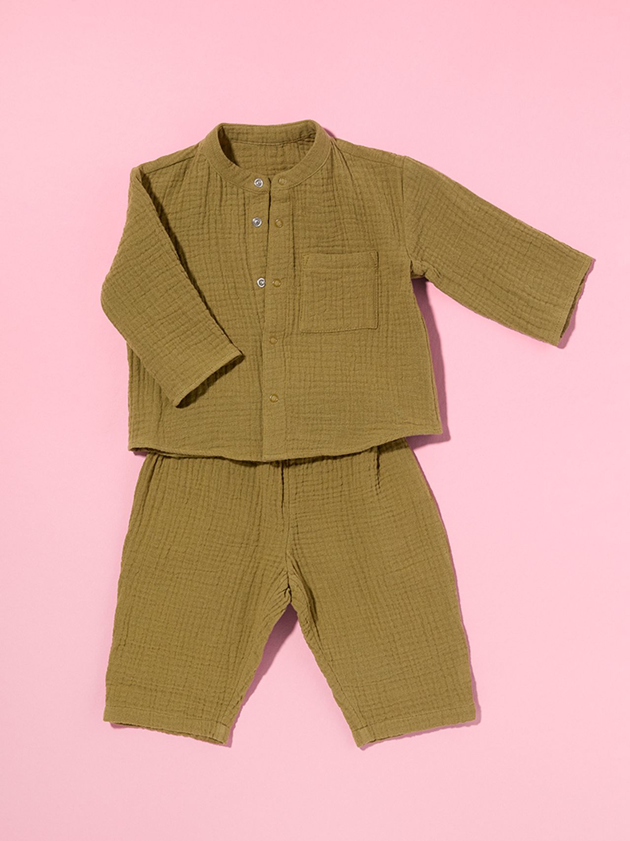 Olive green baby outfit with a button-up top and pants on a pink background. The set features a textured fabric and a small chest pocket.