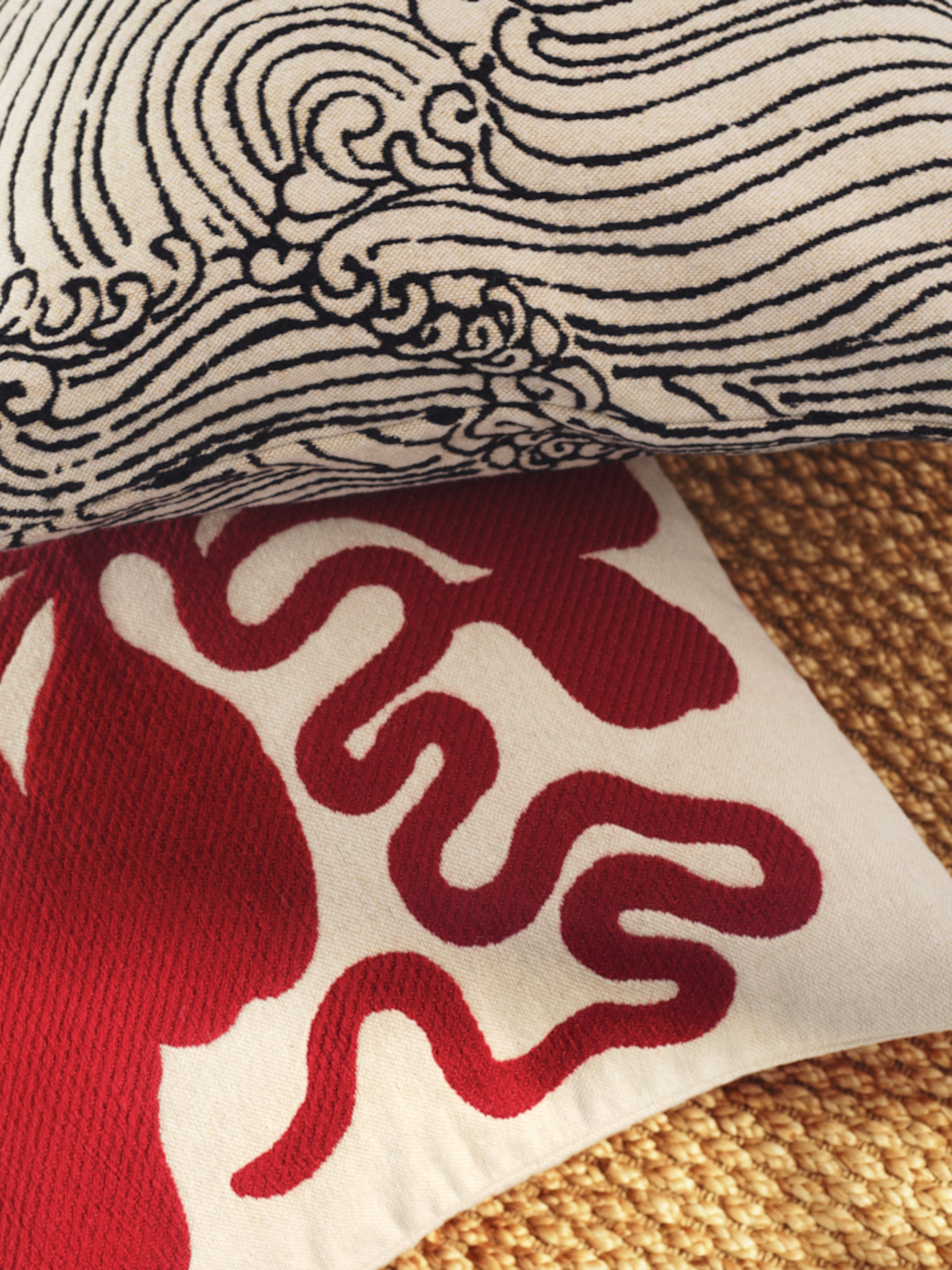 Two patterned pillows, one with black wave designs and the other with red abstract shapes, rest on a textured surface.