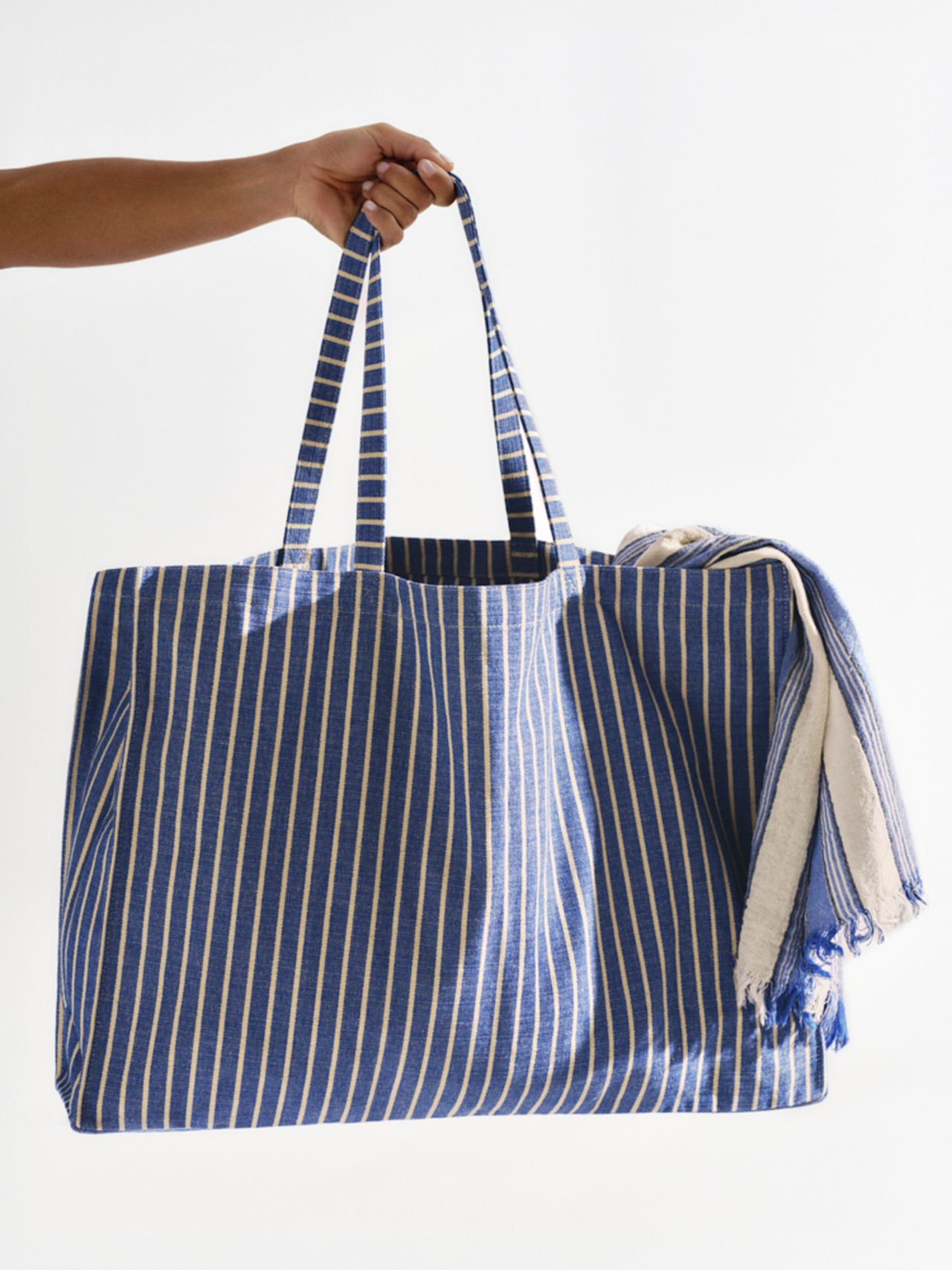 Hand holds a large blue and white striped tote bag with a matching fringed towel partially visible inside.