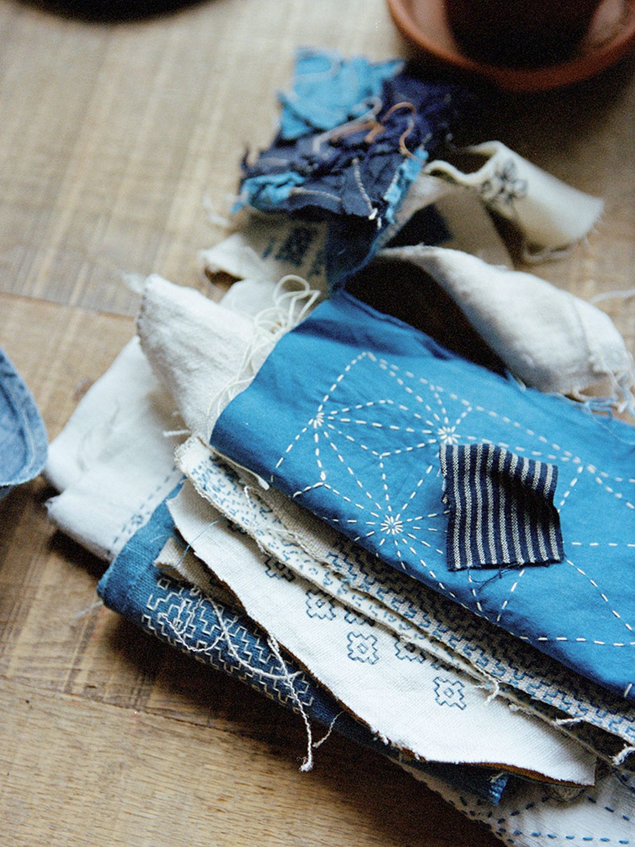 A stack of fabric pieces with blue and white patterns, featuring stitching and embroidery, on a wooden surface.