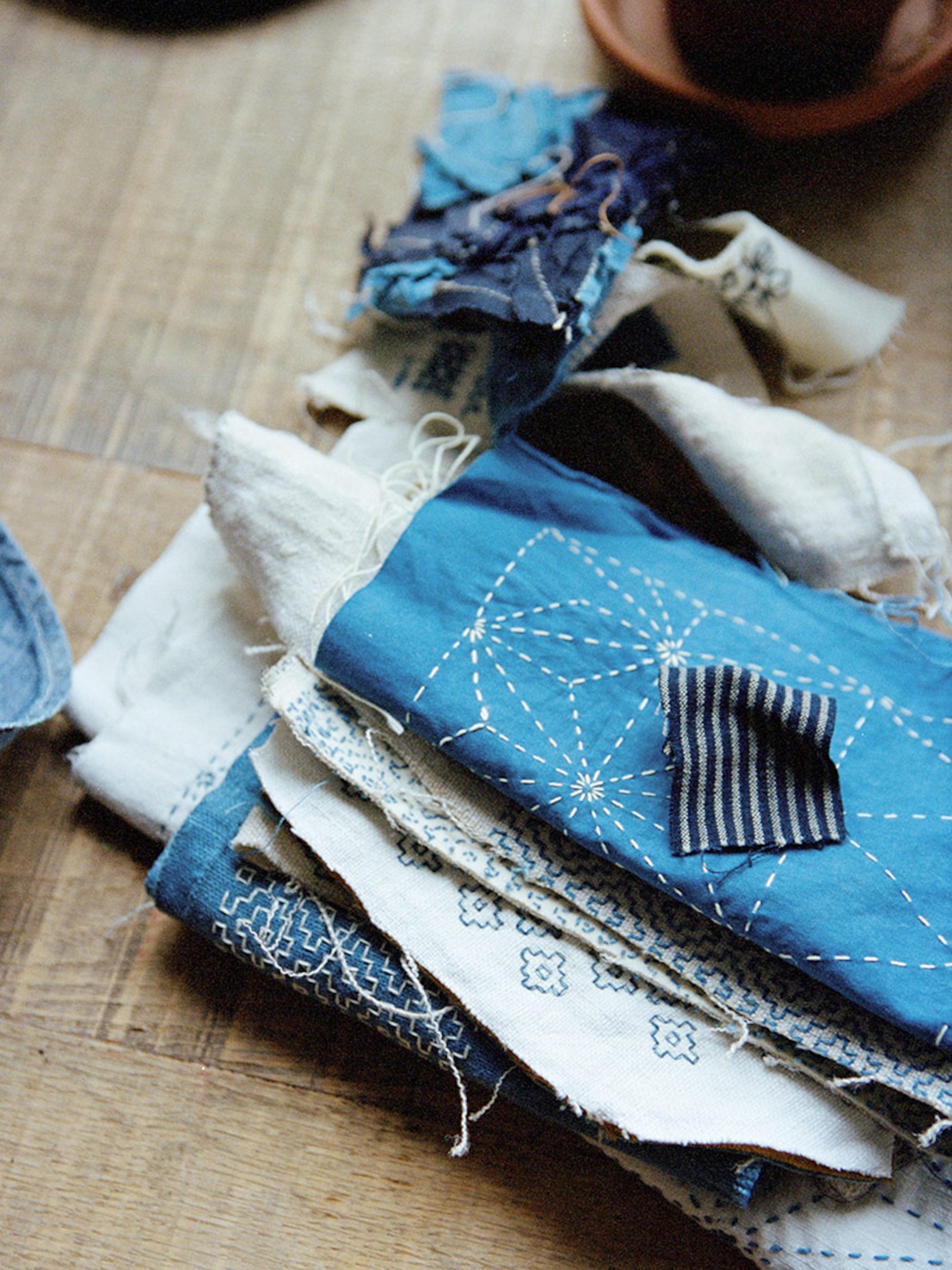 A stack of fabric pieces with blue and white patterns, featuring stitching and embroidery, on a wooden surface.