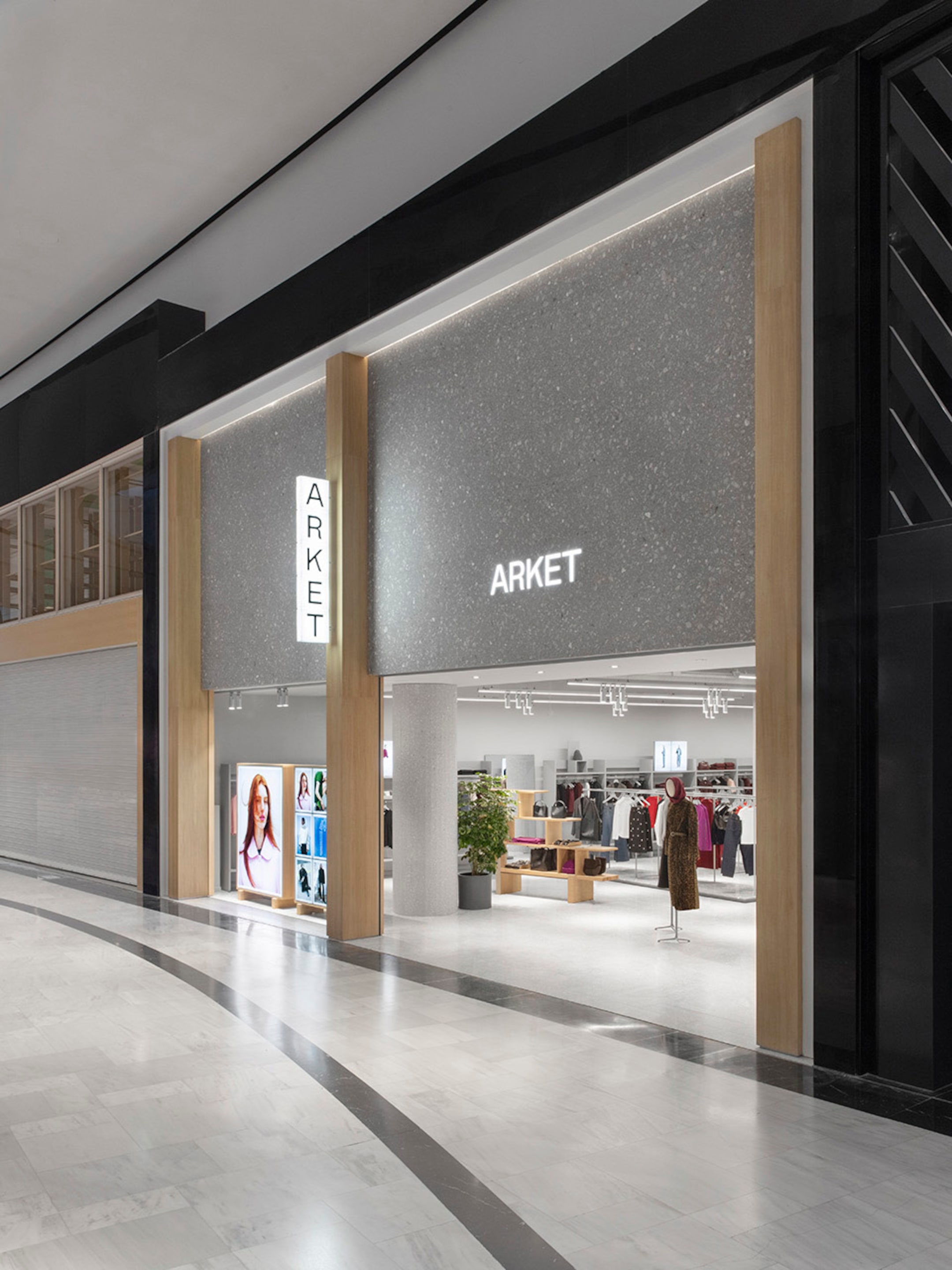 Storefront of ARKET in a mall, featuring large glass windows, minimalist design, and clothing displays.
