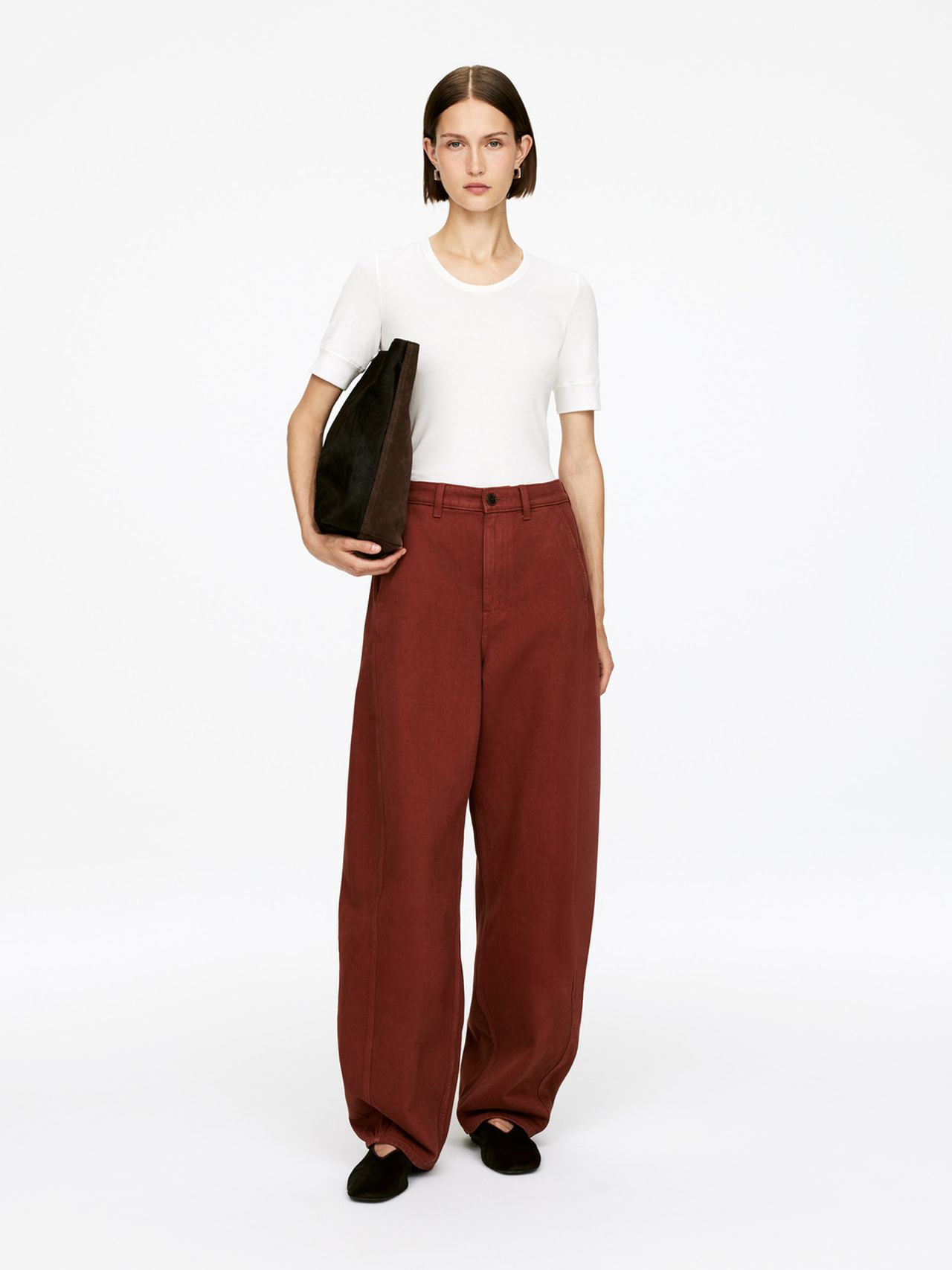 Person wearing a white shirt and wide-legged red pants, holding a black bag, standing against a plain white background.