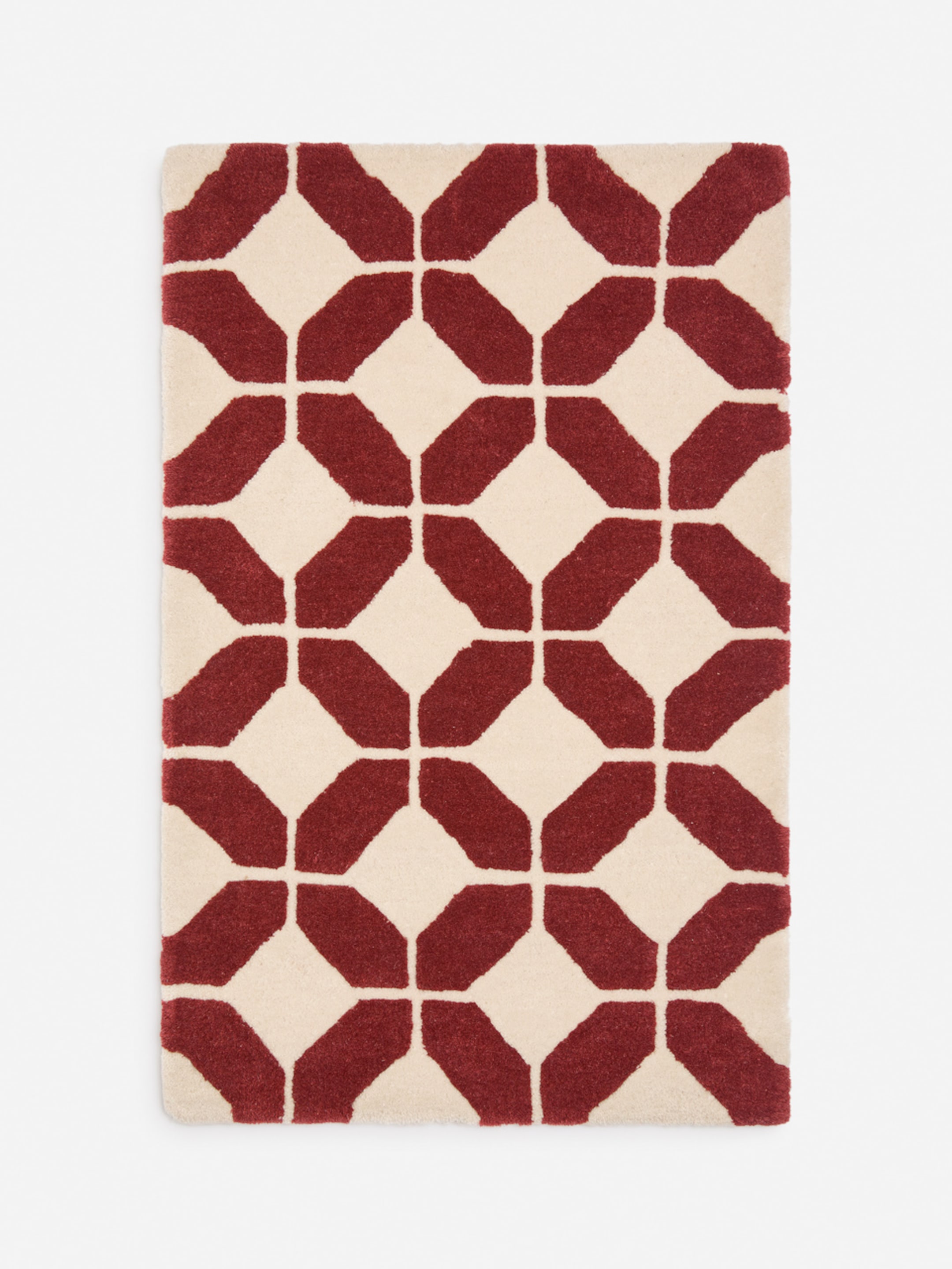 Rectangular rug with a geometric pattern of red and white shapes forming a repetitive design on a light background.