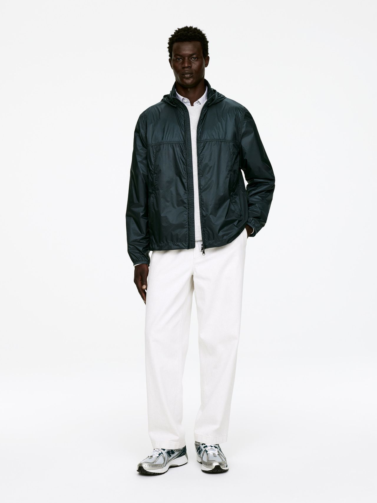 Person wearing a dark jacket, white pants, and sneakers, standing against a plain white background.