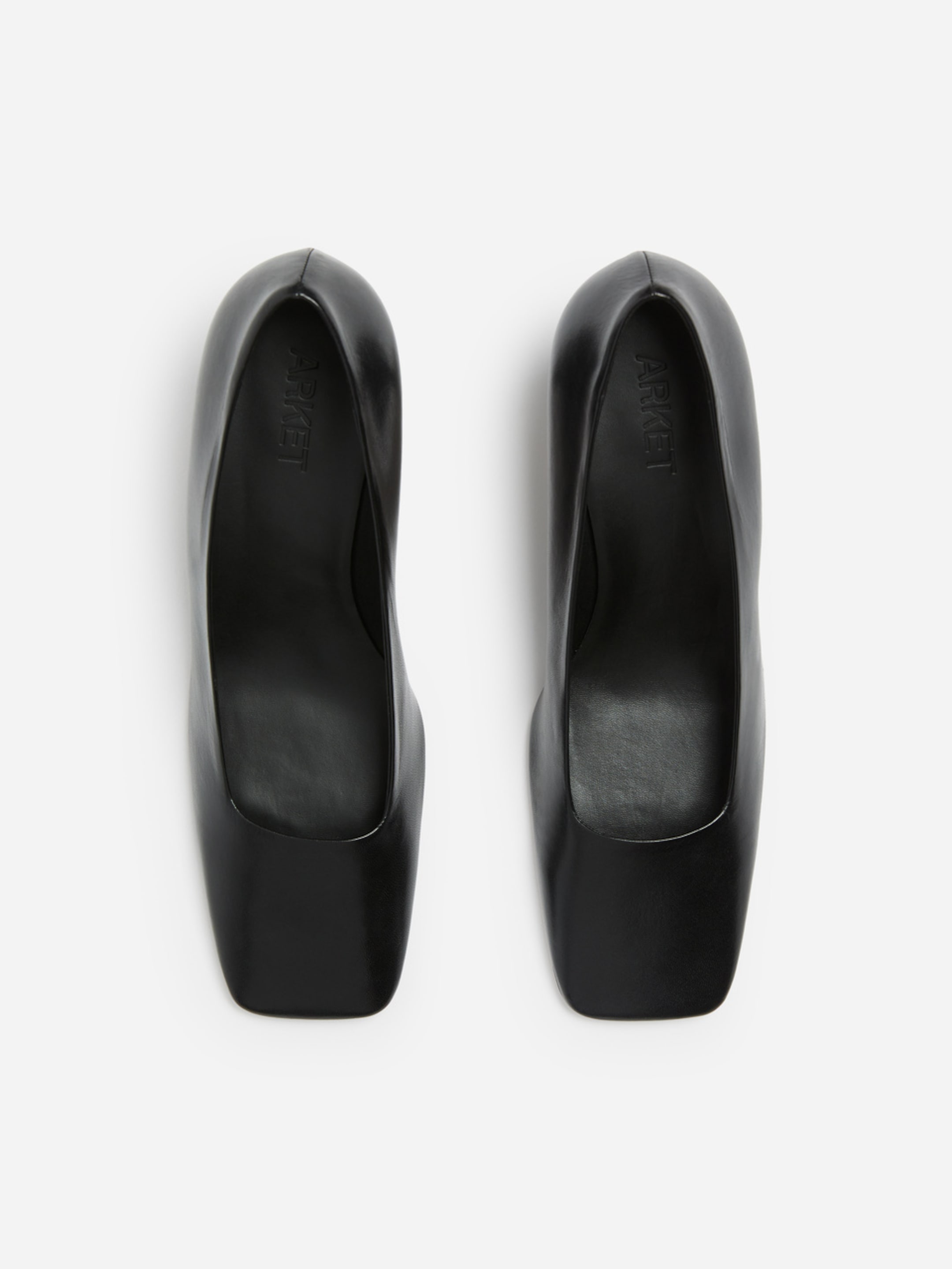 Top view of a pair of black, minimalist, square-toed heels with a smooth surface on a white background.