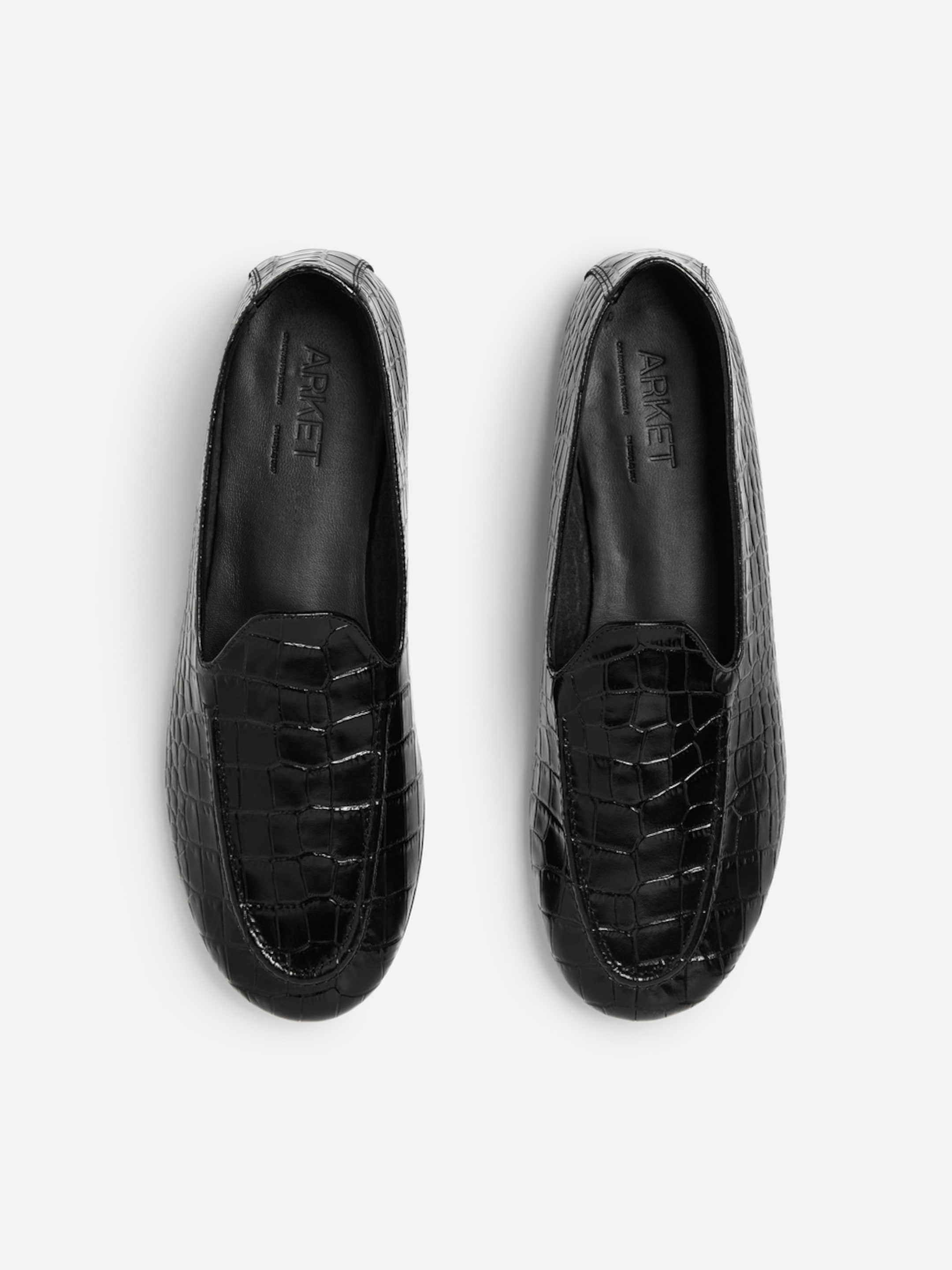 Pair of black loafers with crocodile-patterned texture, viewed from above on a white background.