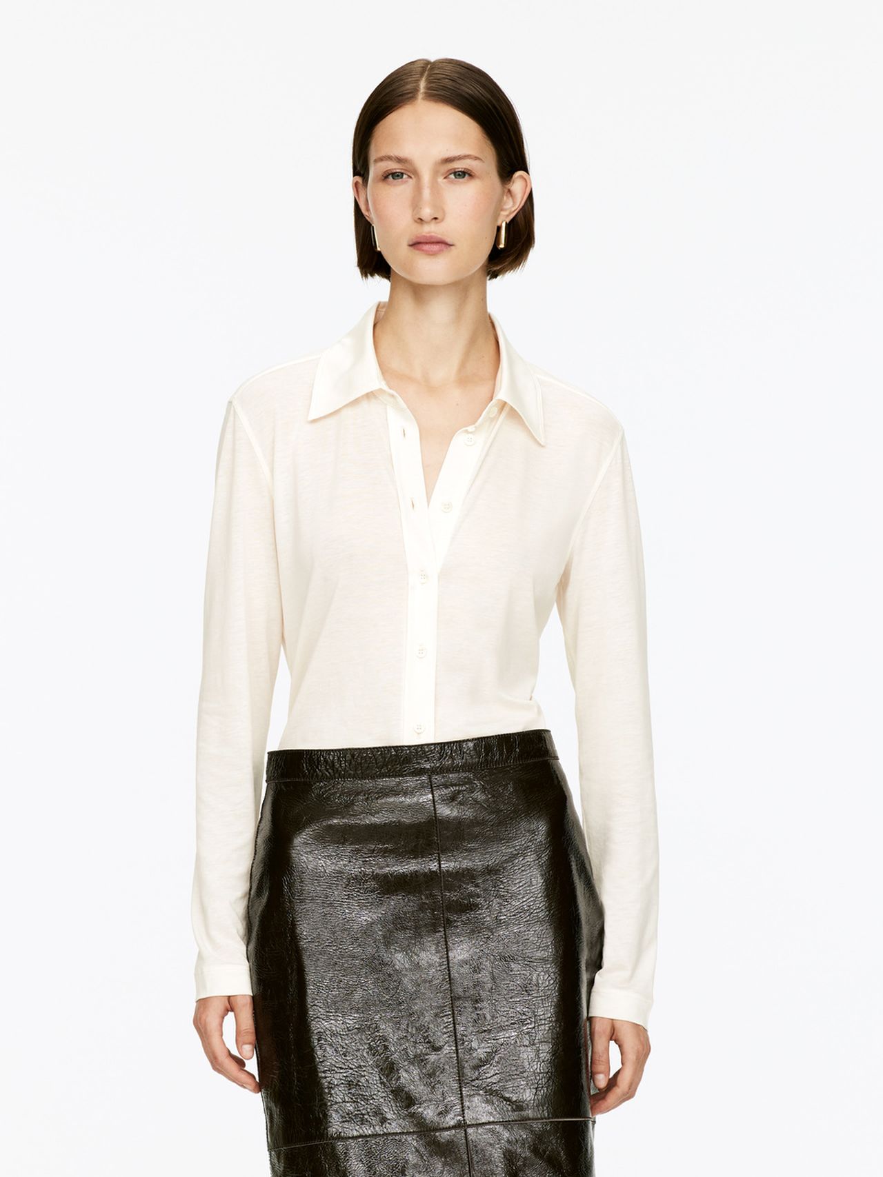 Woman wearing a white button-up shirt and a black leather skirt, standing against a plain white background.